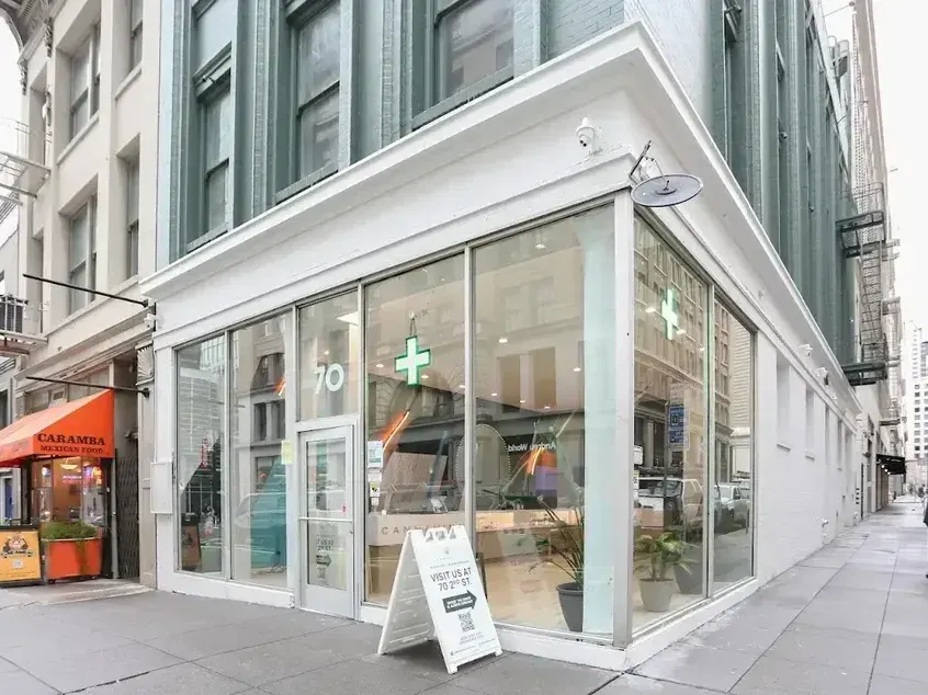Corner storefront with glass windows and green cross sign, urban street view